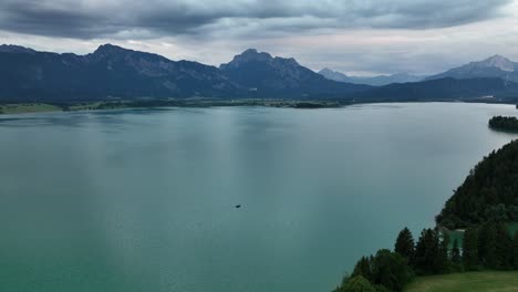 aerial of a little boat sailing on a big lake with mountains in the background, aerial flight backwards