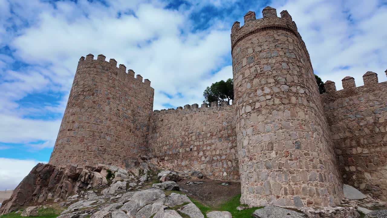 Ampia veduta delle storiche mura medievali di Ávila, Spagna, che si estendono su una collina erbosa sotto un cielo nuvoloso e drammatico, una delle città fortificate meglio conservate d'Europa e un sito patrimonio UNESCO