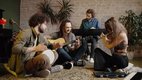 group of happy friends playing music together at home, sitting together on floor, enjoying sound of rehearsal