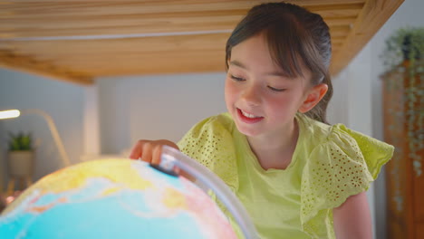 girl in bedroom lying on bed looking at illuminated globe