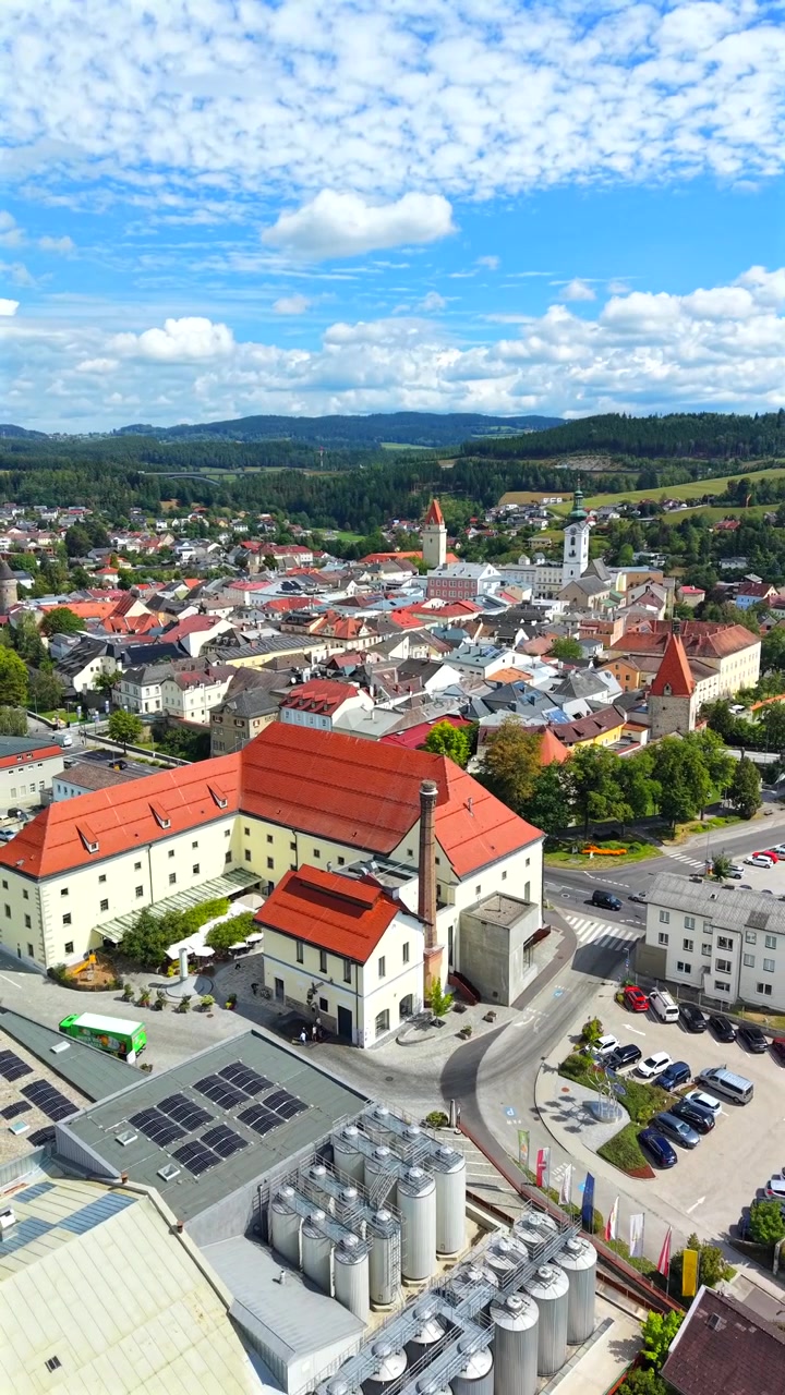Veduta aerea verticale di Freistadt nell'Alta Austria, con serbatoi di birrificio in primo piano e la città storica con le torri della chiesa sullo sfondo
