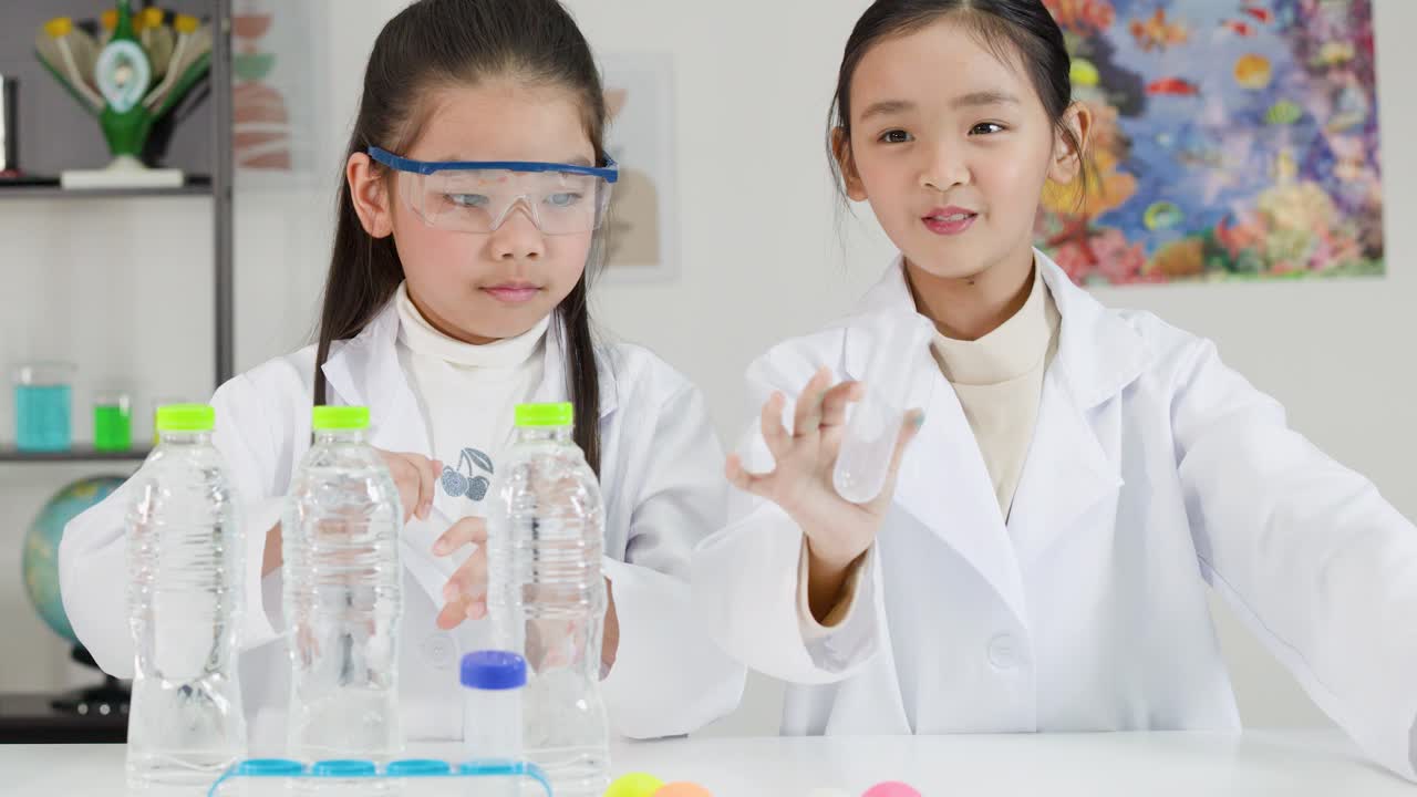 白衣を着たアジア系の学生たちが、ペットボトルとピンポン玉を使って物理実験を行っている