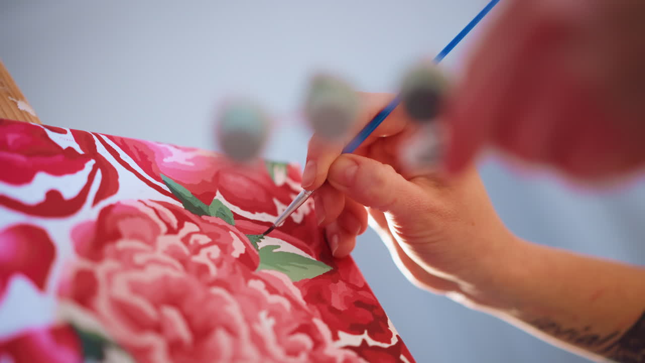 Close Detail Of Artist Hand Painting Leaf Motif On Floral Fabric, Caucasian Maker Applies Green Paint With Small Brush For Precise Textile Decoration, Studio Light Highlights Texture And Pattern