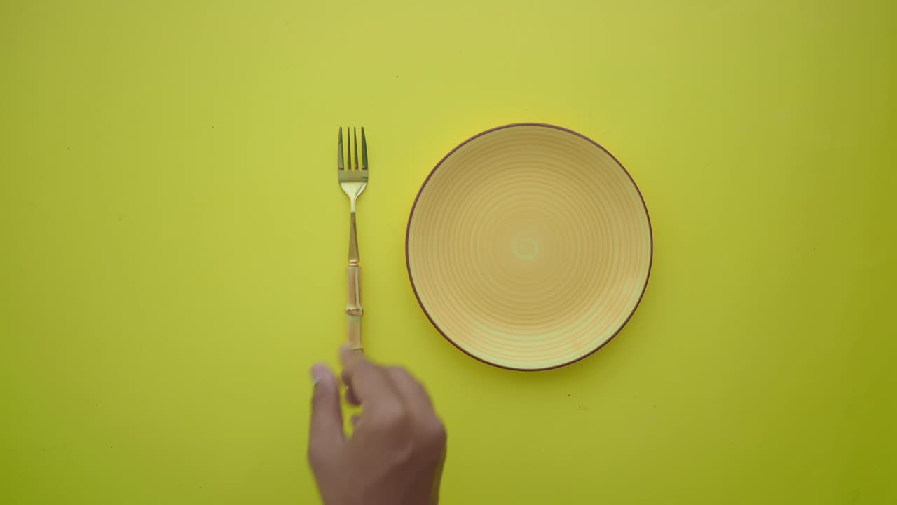 Hand Setting an Empty Plate with Fork and Knife on Yellow Background
