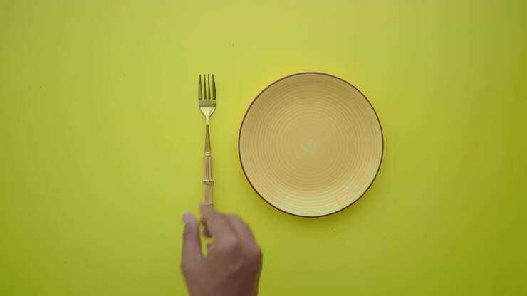 Hand Setting an Empty Plate with Fork and Knife on Yellow Background