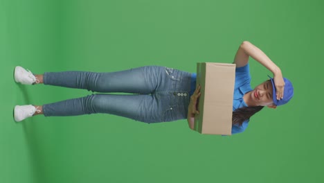 full body of tired asian female courier in blue uniform shaking her head while delivering a carton on green screen background in the studio