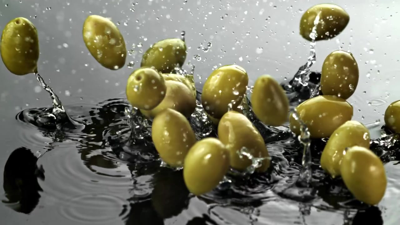 Olive verdi che cadono e schizzano nell'acqua al rallentatore.
