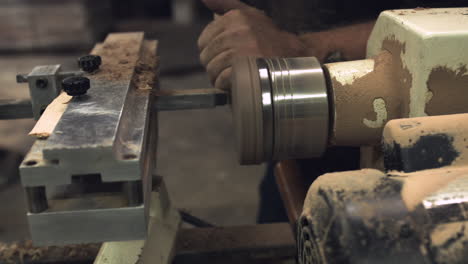 sliding shot of a worker's hands carving wood on a factory lathe