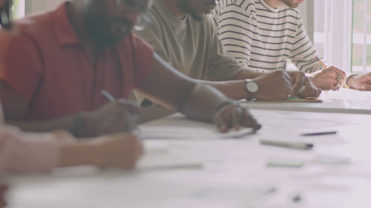 Hands of Migrant Students Writing Test at Desk
