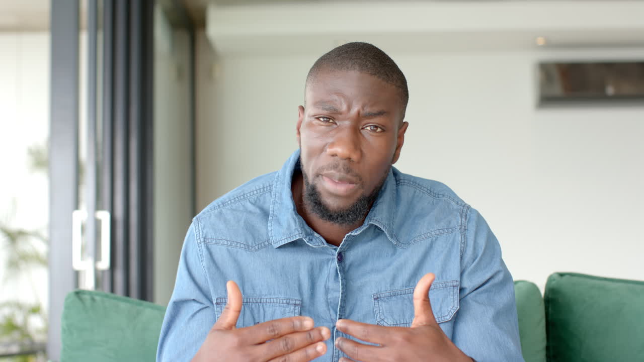 African American man on video call explaining something while sitting on couch