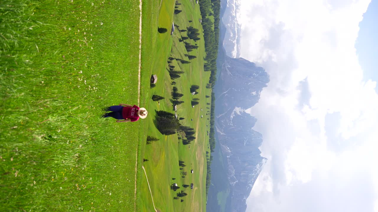 mujer con un sombrero disfrutando del paisaje montañoso del alpe di siusi en medio de un exuberante prado