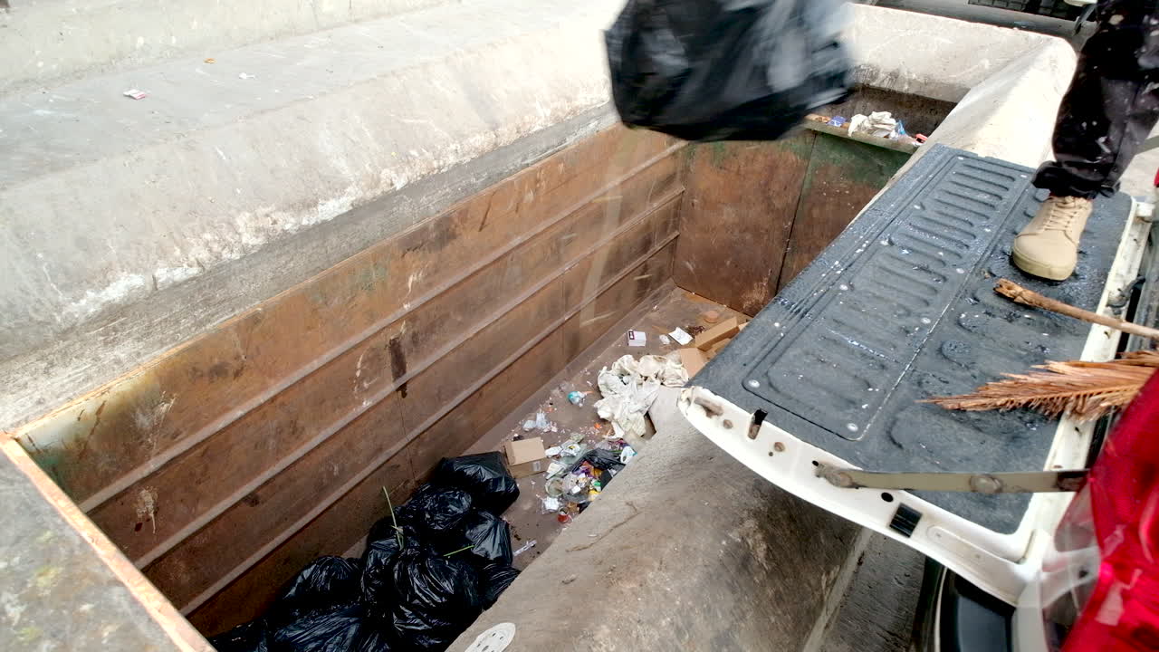 Black garbage bags dumped from back of truck into dumpster at landfill
