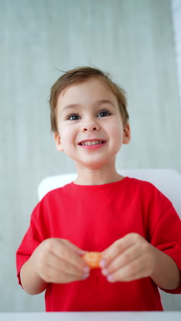 cute caucasian toddler puts a piece of orange into mouth. happy baby eating fruit. low angle view. vertical video.