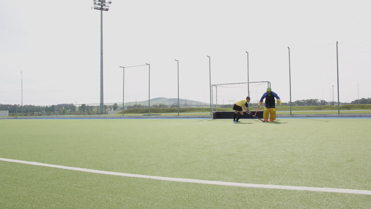 Female hockey player practicing on field, goalie diving to block shot