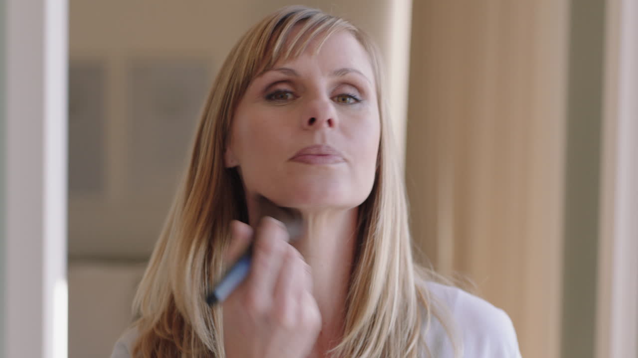 retrato hermosa mujer rubia aplicando maquillaje preparándose en casa mirándose en el espejo disfrutando de la preparación matutina tez natural suave