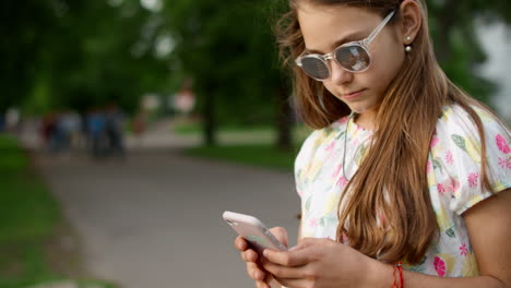 cheerful girl playing games on phone in park. playful girl using smartphone