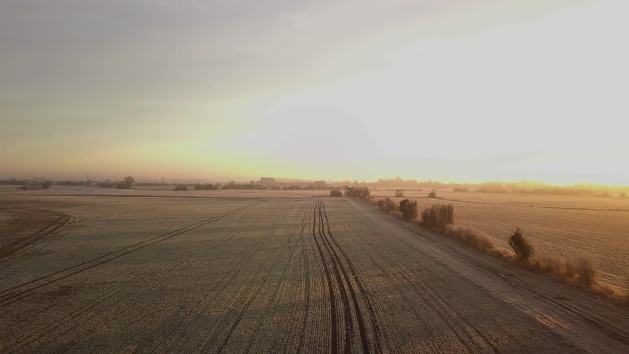 Drone flies across frosty fields with tractor wheel marks