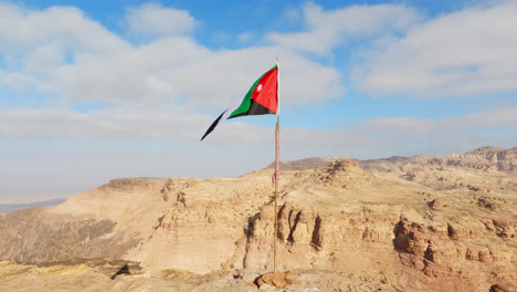 la bandera de jordania ondeando en el viento sobre el acantilado de piedra arenisca del desierto