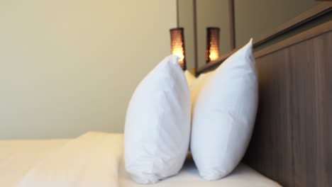 Contemporary-tropical-interior-of-a-hotel-bedroom-with-mirrors,-wooden-lamps-and-headboard-over-a-bed-with-white-linen