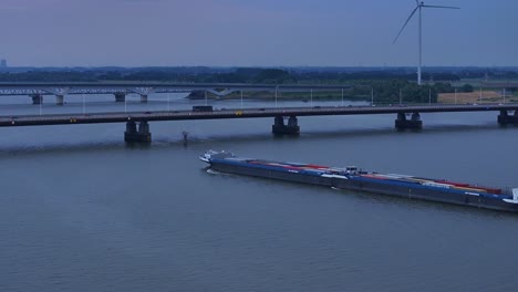 a cargo ship with containers passes under a busy bridge