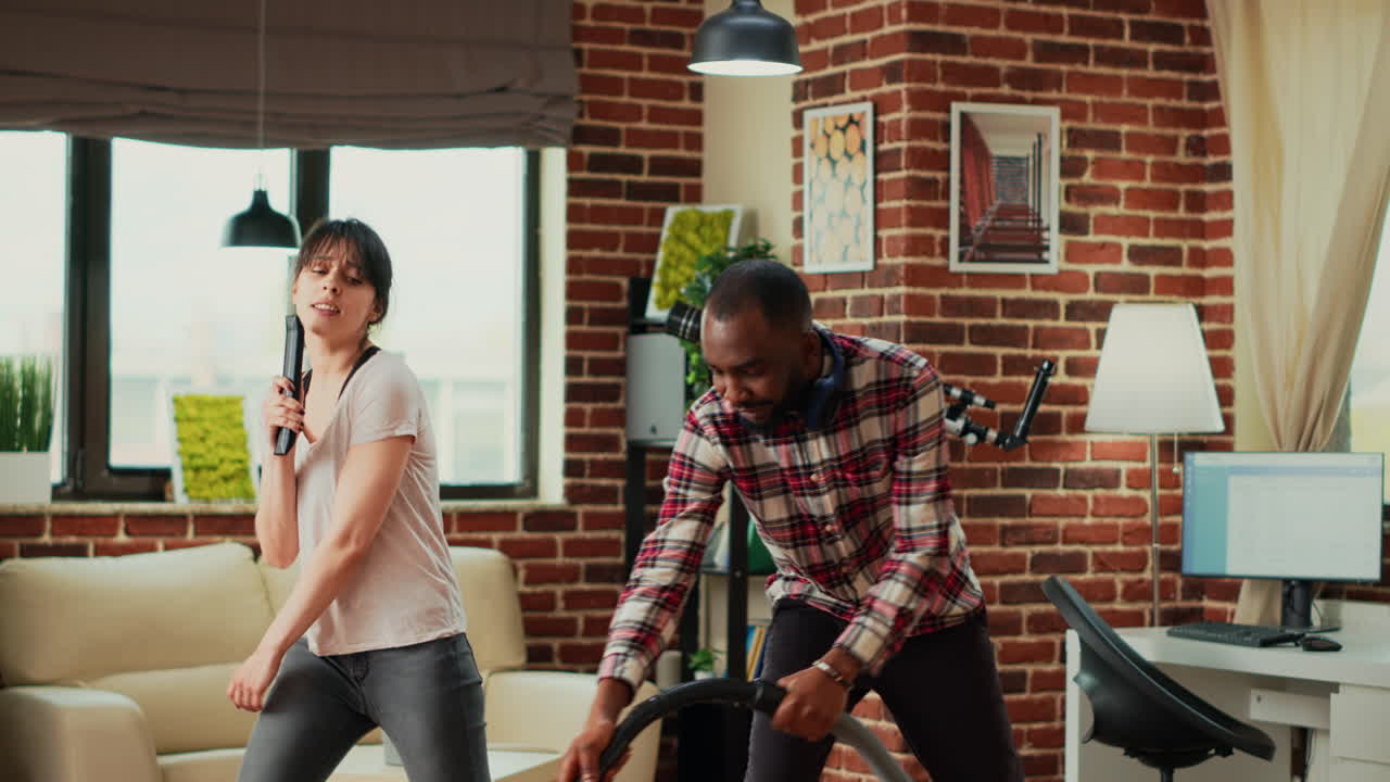 Interracial partners having fun cleaning room with vacuum cleaner and mop