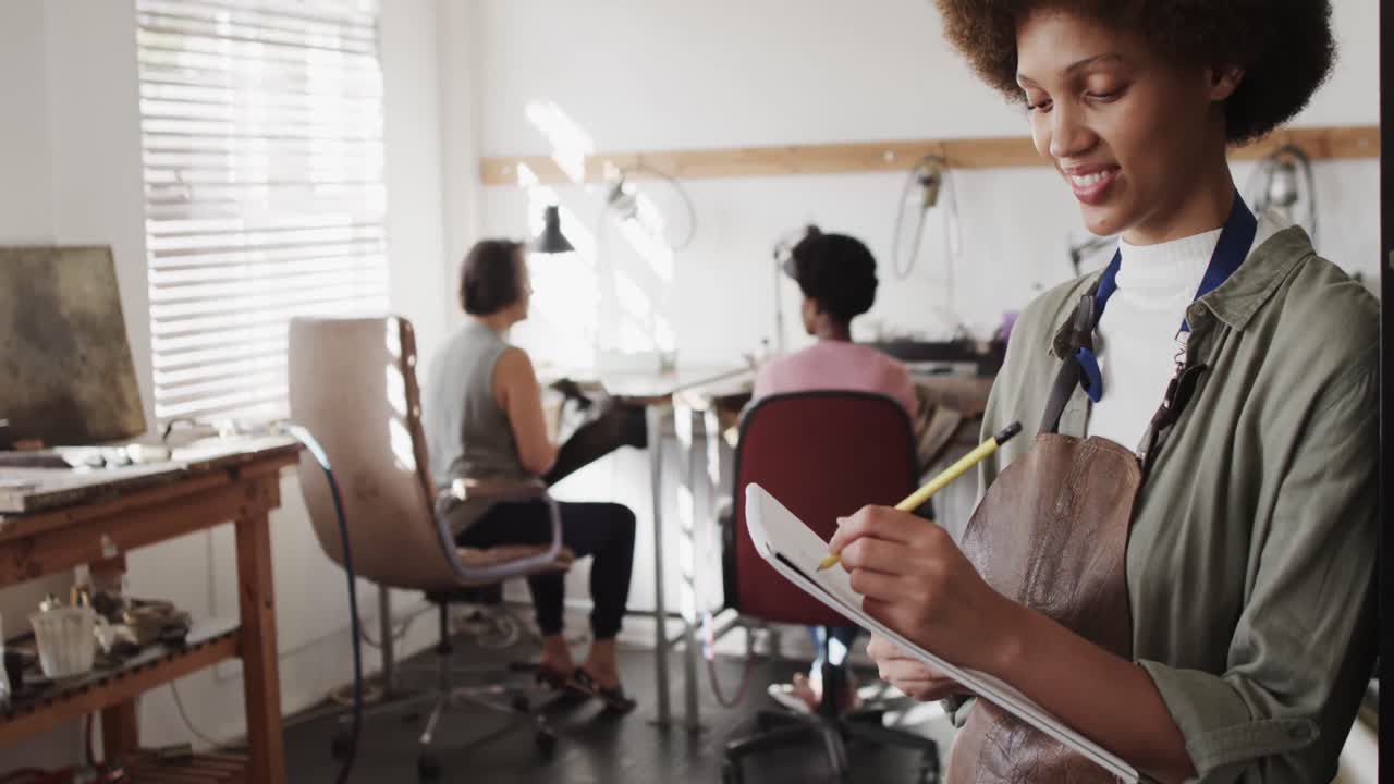 retrato de una feliz trabajadora biracial escribiendo en un taller en un estudio de joyas en cámara lenta