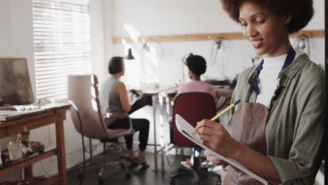 Portrait of happy biracial female worker writing in workshop in jewellery studio in slow motion
