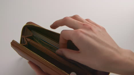 a caucasian woman's hands opening a brown wallet, pulls out a $20 american bill, and places it on the table