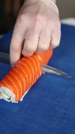 un chef de sushi preparando un rollo de salmón.