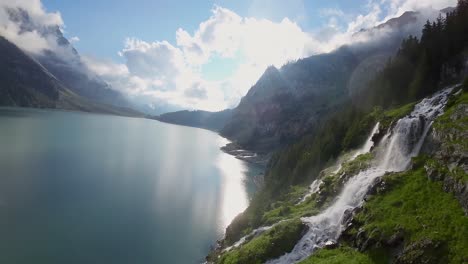 Vuelo-Aéreo-Junto-A-Una-Hermosa-Cascada-Grande-En-Un-Paisaje-Montañoso,-Drones-Volando-Sobre-Un-Lago-Azul---Lago-Oeschinen,-Suiza