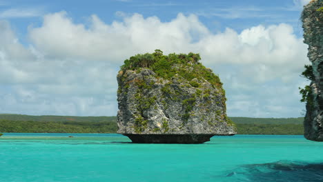 pov revealing large sea stack from canoe sailing on famous upi bay, isle of pines