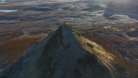 flying over isolated peak in winter early morning with reveal of rugged moorland, coastline and distant mountains beyond