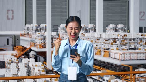 happy asian business woman celebrating using mobile phone in the warehouse