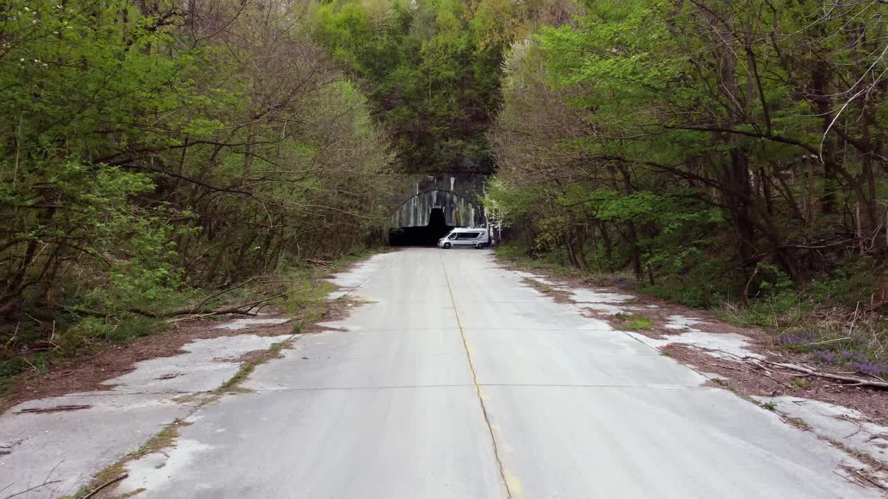 Aerial pullback down remote road from hidden Zeljava airbase entrance carved into a mountain as tour vehicle reverses