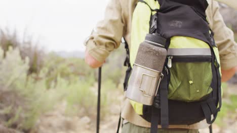 Midsection of caucasian male survivalist trekking through wilderness with backpack and walking poles