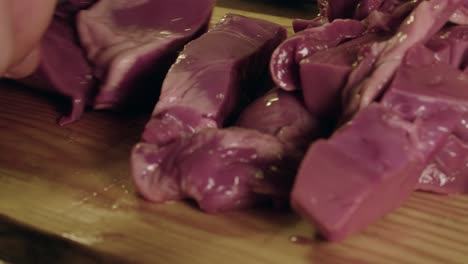 close up view: raw organ meat, pig heart, sliced on wooden chop block