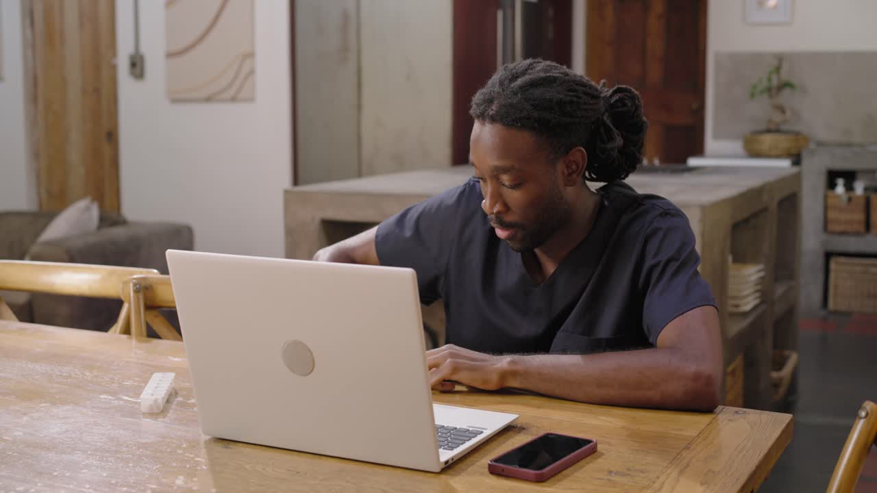 Adult African man in scrubs seeing laptop, checking bottle and swab at wooden table entering data