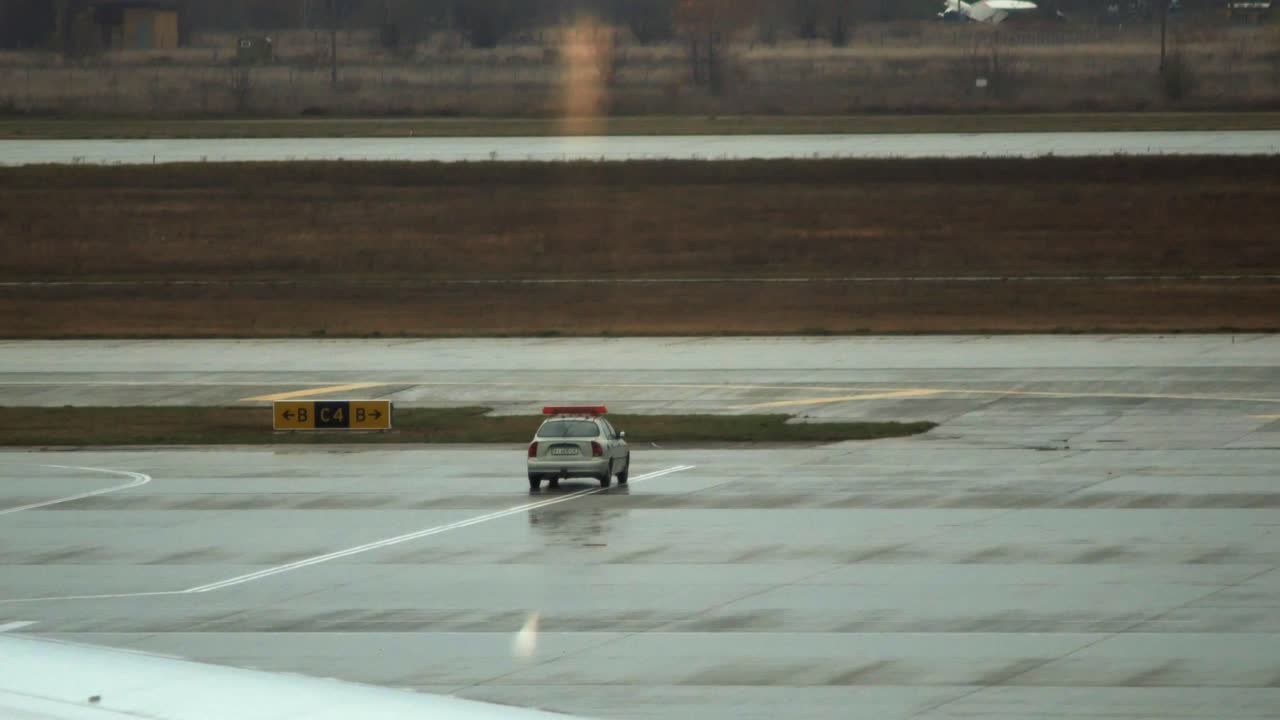 깜박이는 불빛이 있는 차가 공항 앞치마를 통과하고 다른 차가 근처에 주차되어 있습니다.