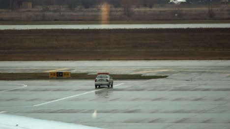 A-car-with-flashing-lights-drives-through-the-airport-apron-while-another-one-is-parked-nearby