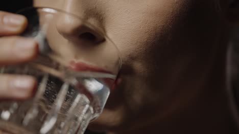 close up shot of a beautiful woman with full beautiful lips drinking a glass of water to quench her thirst against black background in slow motion