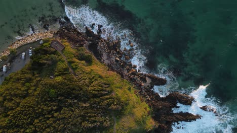 looking down at a scenic rugged coastal headland with surfing waves breaking along the point of a popular holiday spot