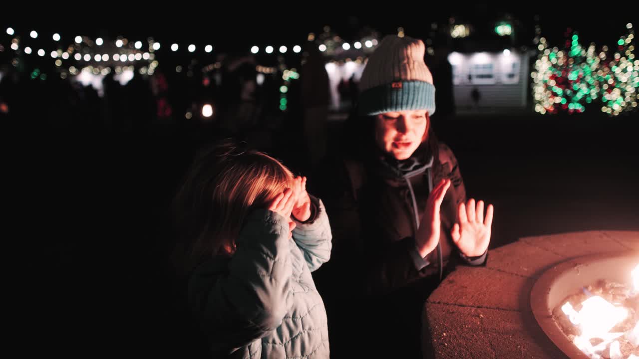 Mother and daughter at a Christmas festival - warming their hands at a firepit at nighttime