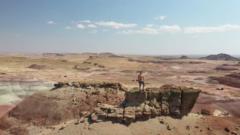 antena de un hombre parado en la roca de la cima de una colina con una vista increíble de las tierras baldías secas del desierto de utah en un día caluroso y soleado, disparo dinámico de drones
