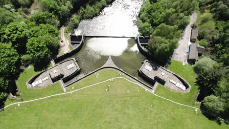 Aerial-View-Of-Spillway-Of-Ladybower-Dam-Flowing-Into-Derwent-River-Surrounded-With-Lush-Green-Forest-In-England,-UK