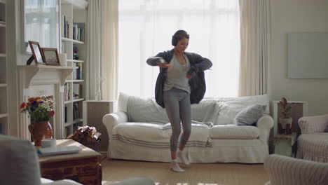 happy young woman dancing at home having fun listening to music wearing headphones enjoying weekend celebration with funky dance moves