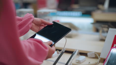 dama vista desde atrás recogiendo una tableta de su soporte en una tienda, la tableta está conectada con un cable de seguridad, mientras que otras tabletas están dispuestas cuidadosamente en la mesa, ella inspecciona el dispositivo de cerca