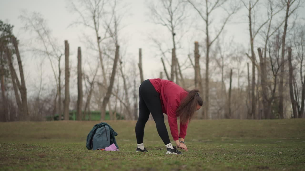 Lady Stretches On Green Grass, Solo Woman Warms Up On Park Lawn, Solitary Woman Prepares For Activity Beneath Cloudy Sky, Woman Gently Limbers Up On Grassy Area With Overcast Clouds Above