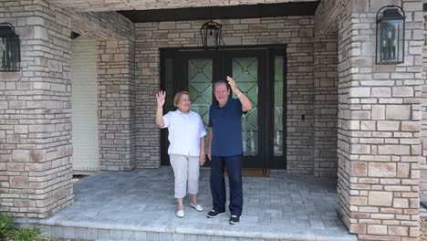 happy older senior couple smiling and waving in front of their new home