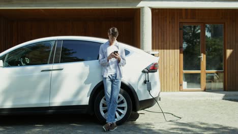 man using phone while charging electric vehicle at home