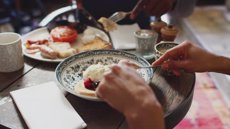 close up of couple at table in traditional english pub eating cooked breakfast and pancakes